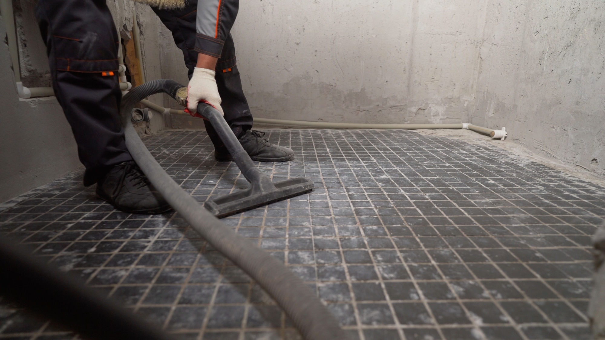 A worker vacuums the bathroom floor before laying. A man vacuums a construction site. Close-up of a cleaner in special clothing holding a brush from an industrial professional vacuum cleaner.